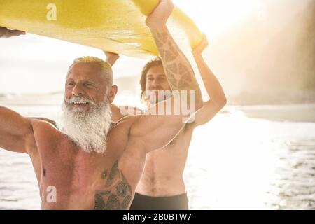 Vater und Sohn, die am tropischen Strand surfen - Familienmitglieder, die Spaß am Extremsport haben - Fröhliches älteres und gesundes Lifestyle-Konzept - Fokus o Stockfoto