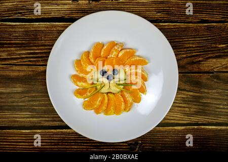 Lustige Löwen-Gesicht-Komposition mit Früchten wie orangefarbener Blaubeere auf Holztisch. Stockfoto