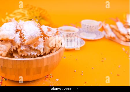 Crostoli, Chiacchiere, Keksekse und duftender Espresso auf gelbem Hintergrund, mit Konfetti und festlichem Dekor. Kaffee und Süßigkeiten für einen traditionellen italienischen Karneval. Kopierbereich Stockfoto