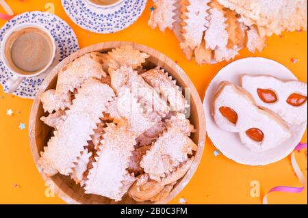 Crostoli, Chiacchiere, Keksekse und duftender Espresso auf gelbem Hintergrund, mit Konfetti und festlichem Dekor. Kaffee und Süßigkeiten für einen traditionellen italienischen Karneval. Flaches Lay. Kopierbereich Stockfoto
