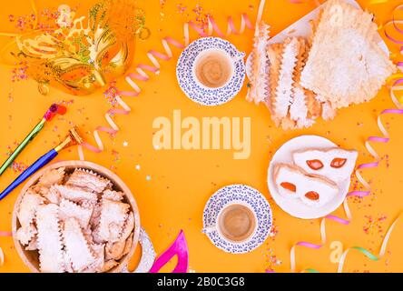 Crostoli, Chiacchiere, Keksekse und duftender Espresso auf gelbem Hintergrund, mit Konfetti und festlichem Dekor. Kaffee und Süßigkeiten für einen traditionellen italienischen Karneval. Flaches Lay. Kopierbereich Stockfoto