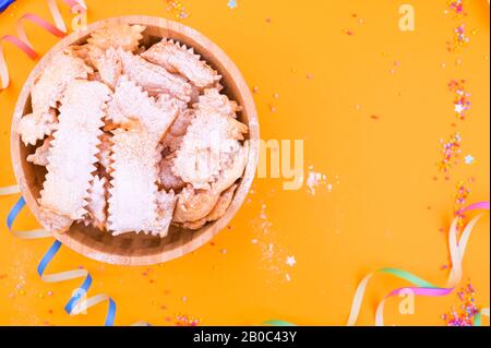 Traditionelle italienische Karnevalsritzer mit Puderzucker - Frappe oder Chiacchiere verstaubt. Süßigkeiten und festliches Dekor auf gelbem Hintergrund. Freier Speicherplatz für Text Stockfoto