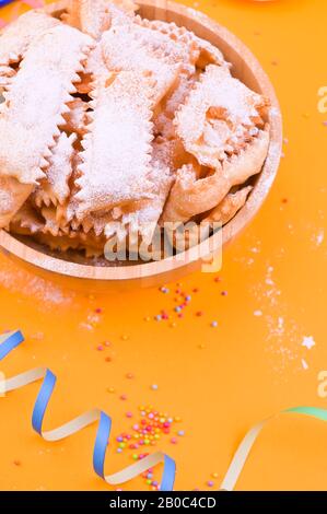 Traditionelle italienische Karnevalsritzer mit Puderzucker - Frappe oder Chiacchiere verstaubt. Süßigkeiten und festliches Dekor auf gelbem Hintergrund. Freier Speicherplatz für Text Stockfoto