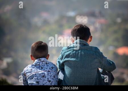 Kalaw, Myanmar - Februar 2020: Idyllische Szene mit zwei jungen Jungen in bunten Hemden, Rücken an Kamera, Blick in die Ferne. Stockfoto