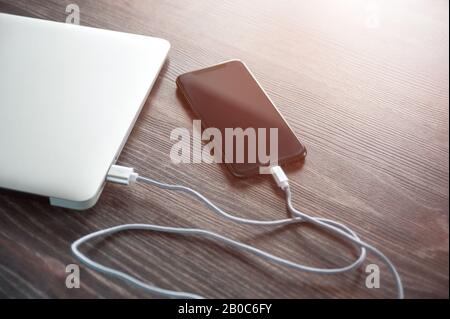 Das Telefon wird von einem Laptop aufgeladen. Aufladen des Telefons, wenn kein Strom vorhanden ist Stockfoto