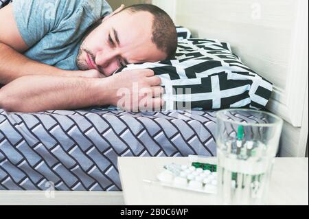 Ein kranker Mann liegt mit einer Temperatur im Bett. Staffel von Erkältungen und Infektionen. Schlafruhe im Krankheitsfall Stockfoto
