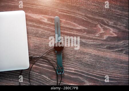 Die elektronische Uhr wird von einem Laptop aufgeladen. Kabelloses Aufladen des Geräts. Stockfoto
