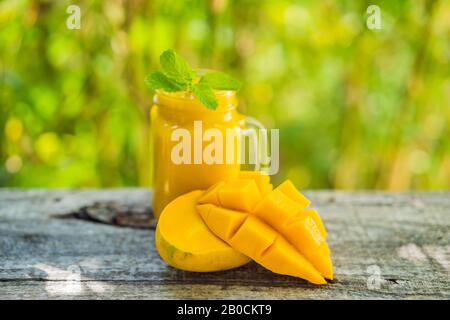 Mango Smoothie in einem Glas Mason Glas und Mango auf dem alten Holzhintergrund. Mango-Shake. Tropisches Fruchtkonzept Stockfoto