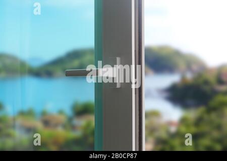 Schiebetür eines Balkons. Nahaufnahme des Schlosses an der Tür mit schöner Hintergrundlandschaft. Weiße PVC-Tür und Sicherheitsglas. Stockfoto