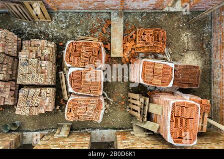 Luftbild der Baustelle für zukünftiges Ziegelhaus, Betonfundament und Stapel gelber Lehmziegel für den Bau. Stockfoto