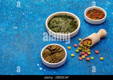 Verschiedene Arten von Lebensmitteln für Aquarienfische. Flocken, Spirulina, Pillen, Mischung. Marineblau Seehintergrund, Kopierraum Stockfoto