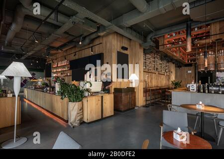 Restaurant im Loft-Stil mit texturierten Holzwänden. Es gibt Tische mit Stühlen und Sofas, viele Regale mit Flaschen, Kaffeebohnenspender aus Glas, Stockfoto