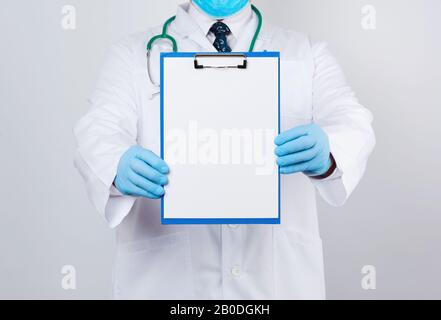 Arzt in einem weißen Mantel, blaue Latexhandschuhe, ein Stethoskop, das an seinem Hals hängt, Arzt, der einen Papierhalter mit einem weißen leeren Blatt hält, Platz für w Stockfoto