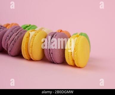 Gelb, violett rund gebackene Makronenkuchen auf pinkfarbenem Hintergrund, Dessert liegt in einer Reihe, nah beieinander Stockfoto