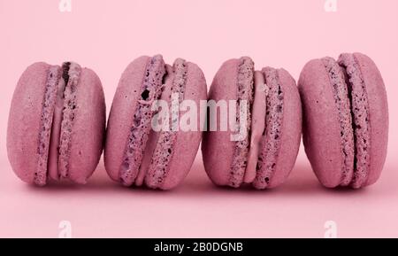 Vier runde lila Mandelmehl Dessertmakarons mit Creme auf pinkfarbenem Hintergrund, köstlicher Kuchen, Nahaufnahme Stockfoto