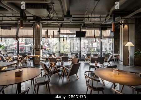 Schönes Kaffeehaus im Loft-Stil mit großen Panoramafenstern und Betonsäulen. Es gibt runde Holztische mit Stühlen und Sesseln, Glaskuppe Stockfoto