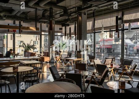 Stilvolles Kaffeehaus im Loft-Stil mit großen Panoramafenstern und Betonsäulen. Es gibt Holztische mit Sofas und Stühlen und Sesseln, gla Stockfoto