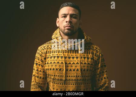 Junger, muskulöser hispanischer Mann, der Hoodie vor braunem Hintergrund trägt Stockfoto