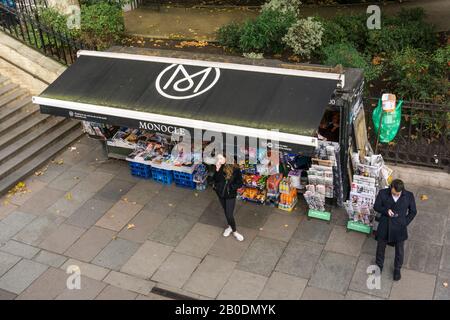 Ein erhöhter Blick auf Menschen, die ihr Handy vor einem Zeitungskiosk in London nutzen. Stockfoto