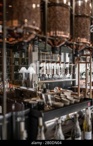 Trendige Kaffeehaus im Loft-Stil mit Betonsäulen. Es gibt viele hängende Kaffeebohnenspender aus Glas, einen Rack mit Kaffeemaschine und Ausrüstung Stockfoto