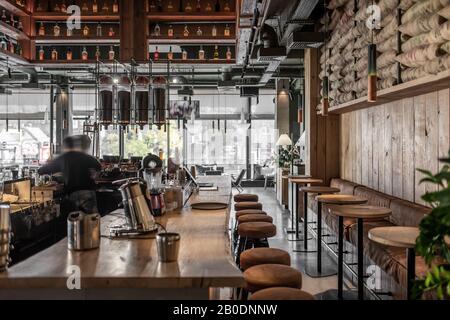 Stilvolles Kaffeehaus im Loft-Stil mit texturierten Holzwänden und Betonsäulen. Es gibt Tische mit Sofas und Stühlen, Regale mit Flaschen, gl Stockfoto