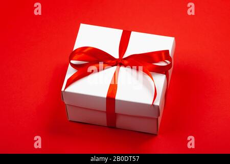 Trendy attraktives minimalistisches Geschenk im roten Hintergrund. Tag der Frauen, Valentinstag, Alles Gute Zum Geburtstag und andere Feiertage. Stockfoto