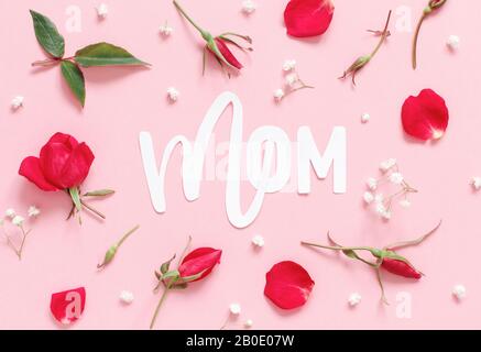 Rote Rosen Blumen und Wort MOM auf hellrosa Hintergrund Draufsicht Stockfoto