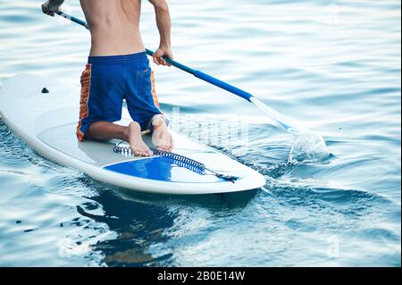 Junger Mann, Der Spaß Hat, Im Meer zu Paddeln. SUP. Guy Training am Morgen auf Paddle Board in der Nähe der Felsen. Stockfoto