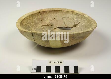Eine Schüssel aus Steingut. Boden und Wand verlaufen konvex. Der Rand ist nach außen gebogen und innen verdickt und schräg abgeflacht. Außen, unter der Kante, eine flache horizontale Nut. Die Schüssel ist an zwei Seiten leicht eingedellt. Hergestellt am Rad. Der Ton ist violett-braun und grün und wird mit Sand und Kalk agglutiniert. Leicht gesintert (kleine gerissene Bläschen in der Oberfläche vergleichen). Außen eine hellgelbe Beschichtung mit orangefarbenem Nubtrnsl31900 Stockfoto