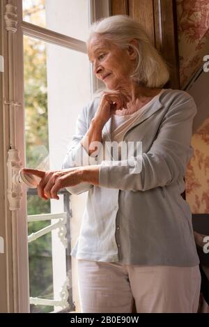 Ältere Frau stehen in der Nähe von Fenster Stockfoto