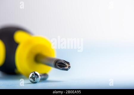 Nahaufnahme des Schraubendrehers sind Kreuz und geeignete Schraube auf hellblauem Hintergrund. Werkzeuge. Kompatibilität. Reparieren. Speicherplatz kopieren Stockfoto