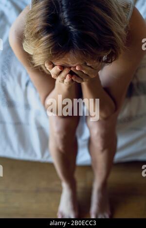 Gestresste Frau auf dem Bett sitzend Stockfoto