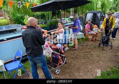 Menschen auf dem Kanalpfad besuchen an einem Sommernachmittag das Gnosall Canal Festival. Besucher, die auf vermoorte Boote blicken und Waren von Händlern kaufen. Stockfoto