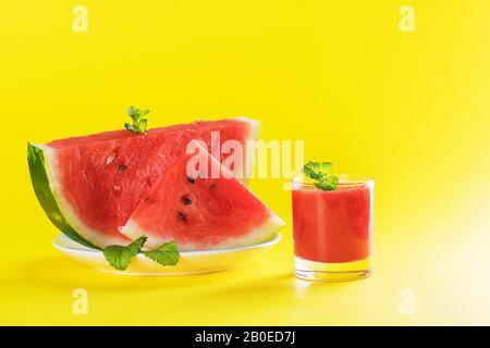 Sommergetränk, Wassermelonen-Smoothie in einem Glas mit frischen Wassermelonenscheiben auf einem Teller auf gelbem Hintergrund, sommerliches gesundes Fruchtgetränk, Nahaufnahme Stockfoto