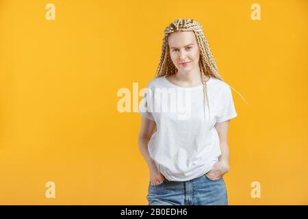 Hipper Mode junge Frau mit Kanekalon in weißem T-Shirt auf gelbem Hintergrund. Stockfoto