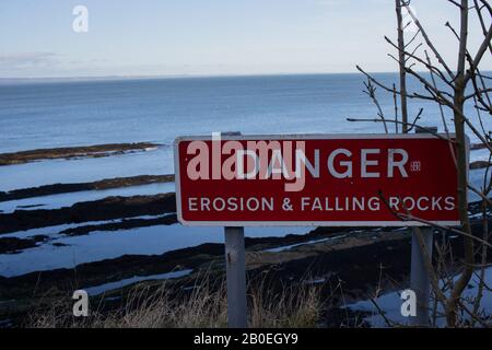 ST ANDREWS, SCHOTTLAND - 17/2/2020 - EIN Zeichen, das vor Gefahr durch Erosion mit der Nordsee im Hintergrund warnt Stockfoto