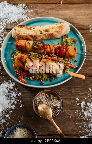 Gemüsekebabs mit Kürbis, Süßkartoffel, Tofu, Champignons und Tomaten werden im Winter mit geröstetem Baguette und Salatbesatz auf einem blauen Teller serviert Stockfoto