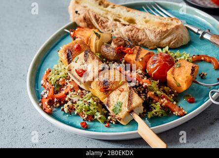 In der Nähe servieren wir Gemüse-Tofu-Kebabs mit verschiedenen Gemüse auf einem Bett aus Salatgrüns mit Quinoa oder Couscous für eine gesunde vegetarische Mahlzeit Stockfoto