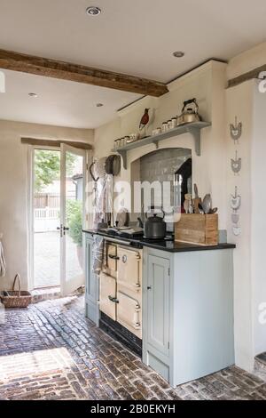 Hellblaue Einbauküche mit Kopfsteinpflasterboden Rayburn in Küche in Farrow & Ball's Matchstick mit original gepflastertem Boden. Stockfoto