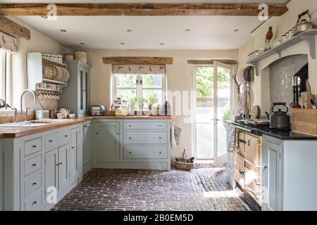 Hellblaue Einbauküche mit Kopfsteinpflasterboden Rayburn in Küche in Farrow & Ball's Matchstick mit original gepflastertem Boden. Stockfoto