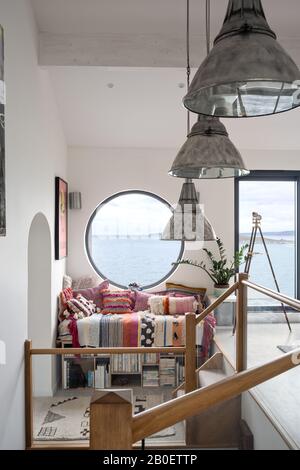 Großes Porthole-Fenster über Tagbett und Lagerbank in geteilter Renovierung der 1960er Jahre mit Blick auf den Strand von Fistral Stockfoto