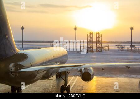 Das Flugzeug steht bei Sonnenaufgang im Hangar. Ein frostiger Tag und ein Flugzeug, Blick von hinten. Vorbereitung des Flugzeugs auf den Abflug. Winterflugzeug bereit Stockfoto