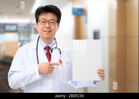 Ein männlicher Arzt, der eine Meldungsplatine in einem Krankenhaus hält. Stockfoto