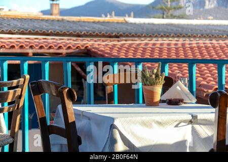 Ein leerer Tisch, der bereit ist, Gäste zum Abendessen in der griechischen Taverne mit Blick auf alte Dächer auf Kretas, Griechenland, willkommen zu heißen Stockfoto