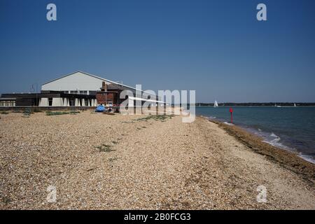 Blick auf den Calshot Activity Center Hanger und den Steinmetzstrand, der zum Solent Water führt. Das Zentrum bietet Klettern, Indoor-Biking und Skicenter. Stockfoto