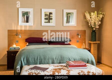 Moderne Kunst über dopublem Bett mit hellgrüner Decke und Büchern auf Rindsleder Fußhocker. Stockfoto