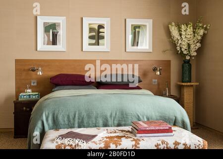 Moderne Kunst über dopublem Bett mit hellgrüner Decke und Büchern auf Rindsleder Fußhocker. Stockfoto