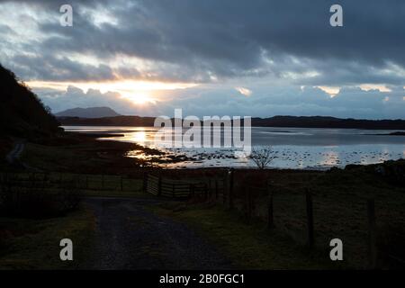 Sonnenuntergang über der Ardmaddy Bay, Schottland am Weihnachtstag, während die letzten Sonnenstrahlen auf das Wasser fallen, was eine Goldspiegelung gegen die Dunkelheit liefert Stockfoto