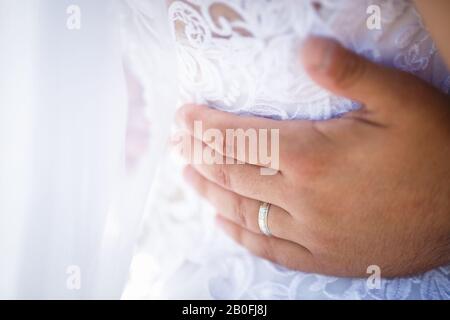Bräutigam umarmt die Frau, die Hände der Neuvermählten. Kleid mit offenem Rücken Stockfoto