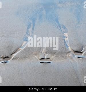 Abstrakte detaillierte Gezeitenmuster und blaue Himmelsreflexionen im Sand bei Ebbe am Penbryn-Strand im Südwesten von Wales UK Stockfoto